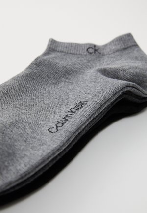 Calzini grigi realizzati in tessuto a maglia fine, con un logo nero "Calvin Klein" vicino al gambale, caratterizzati da una texture liscia e senza motivi visibili.