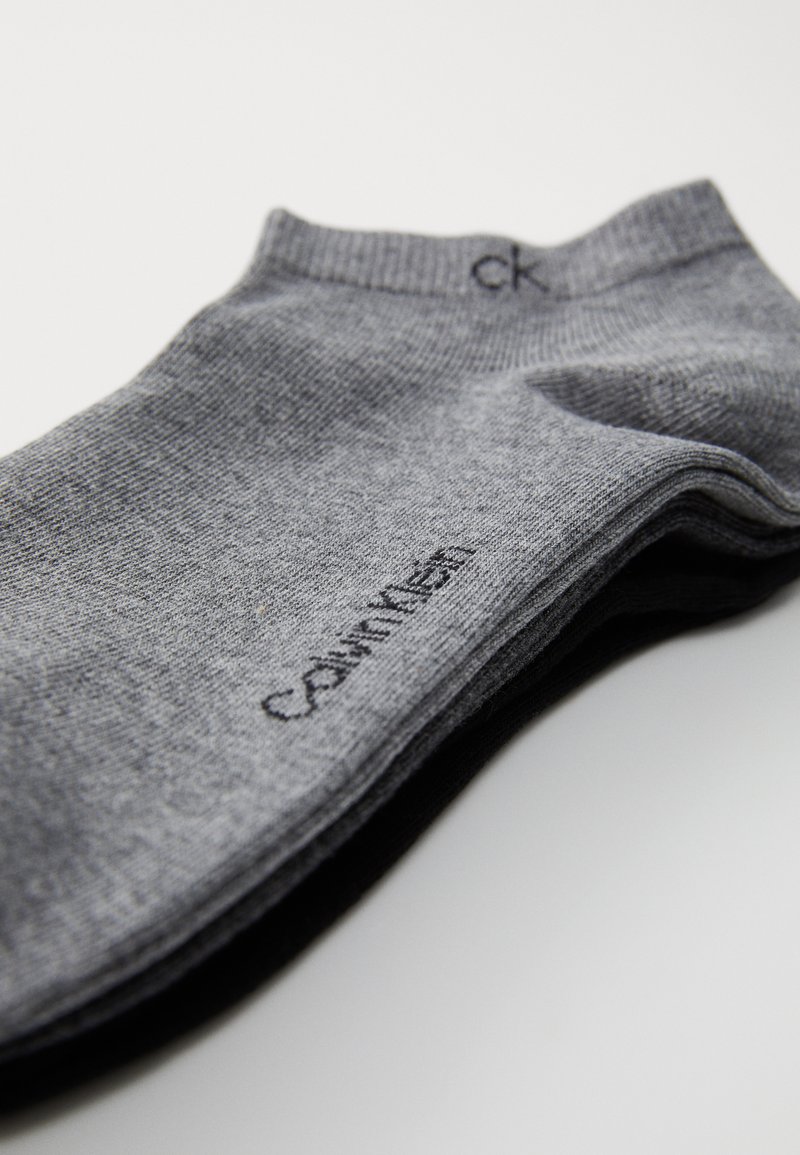 Calzini grigi realizzati in tessuto a maglia fine, con un logo nero "Calvin Klein" vicino al gambale, caratterizzati da una texture liscia e senza motivi visibili.