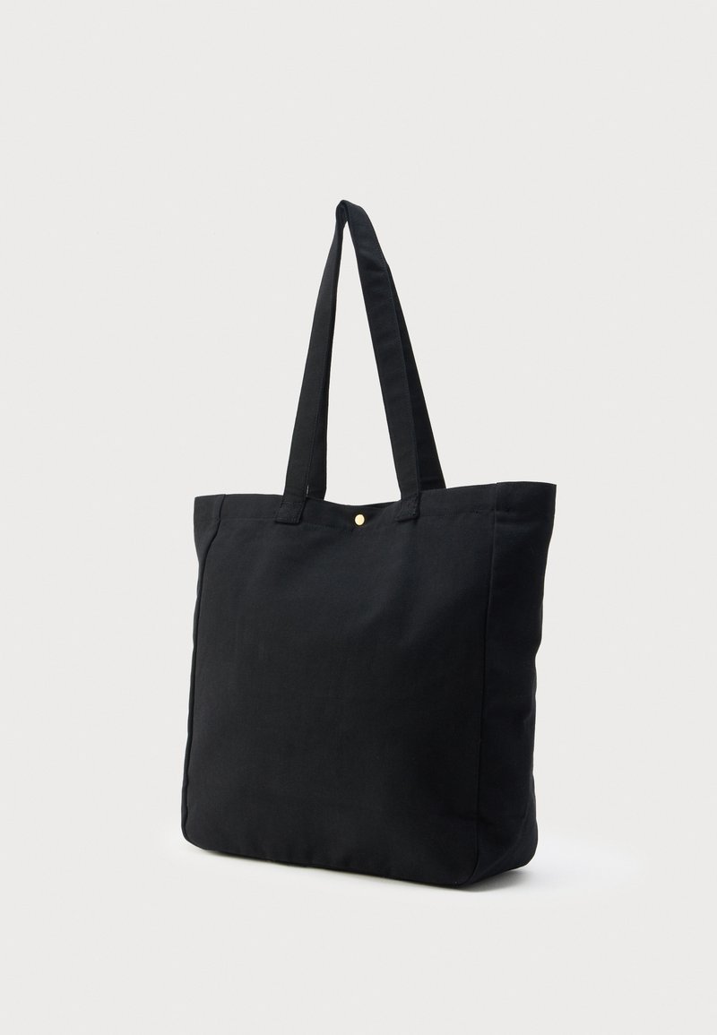 Black fabric tote bag with two shoulder straps and a small gold snap button closure at the top center.