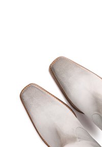 Cizme cu gleznă din suede, de culoare gri deschis, cu o textură netedă, vârfuri pătrate și cusături maro contrastante de-a lungul talpilor.