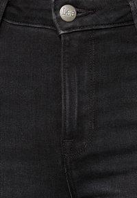 Svarta denimjeans med hög midja, en silverknapp med "Lee"-logotyp och diskreta sömnadsdetaljer p å fickorna.