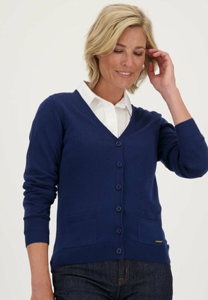 Marineblauwe cardigan, knopen-voorzijde ontwerp, V-hals, ribgebreide manchetten en zoom, twee voorzakken, zachte textuur, gecombineerd met een witte blouse met kraag.