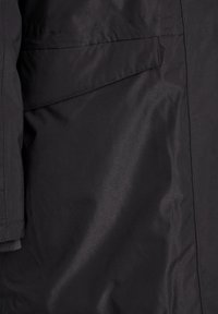 Crna jakna s glatkom, vodootpornom tkaninom, bočnom džepom i teksturiranim manžetama. Dizajn naglašava funkcionalnost i jednostavnost.