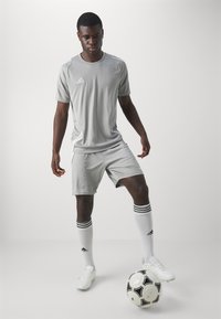 Šedý športový dres a šortky s bielymi akcentmi, bielo pruhované čierne ponožky, biele kopačky a čierno-biela futbalová lopta.