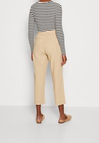 Top a maniche lunghe a righe bianco e nero abbinato a pantaloni beige, corti e larghi. L'outfit presenta una vita elasticizzata.