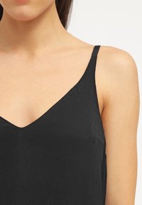 Černý top bez rukávů s V-výstřihem, který má hladkou strukturu a tenké ramínka. Design zdůrazňuje minimalistický styl.