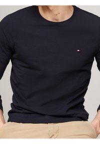 Navy long-sleeve shirt made of soft cotton. Crew neckline, fitted design. Features a small embroidered logo in red, white, and blue on the chest.