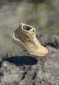 Beige túracipő párnázott gallérral, texturált felsőrésszel és világosbarna talppal. Fűzős kialakítású, látható logóval.