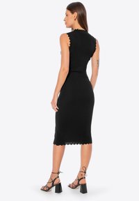 Abito midi nero in maglia con bordi ondulati, silhouette aderente e design senza maniche. Abbinato a tacchi neri con cinturini.