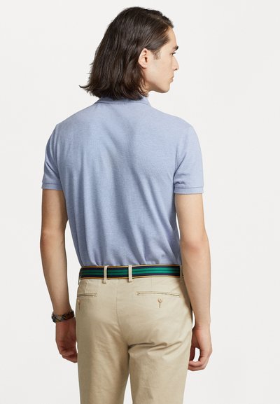 Tricou polo de culoare albastru deschis, cu mânecă scurtă, văzut din spate, asociat cu pantaloni bej și o curea în dungi, cu accente verzi, albastre și negre.