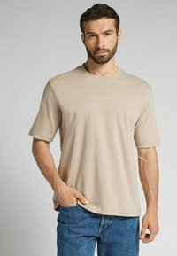 Beige bavlněné tričko s krátkým rukávem, kulatým výstřihem, volným střihem a jemnou strukturou, doplněné modrými džíny.