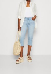 Kevyt pellavapaita, valkoinen toppi, vaaleansininen lyhytlahkeinen farkut, kudottu olkikassia ja beigellä alustalla varustetut sandaalit, joissa on hihnat.