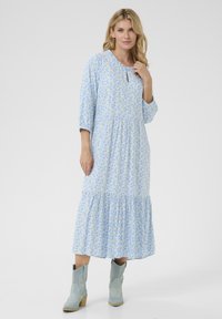 Zila ziedu maksi kleita ar trim ceturtdaļa piedurknēm, viļņotu apakšmalu un atvērtu kakla detaļu. Valkāta ar gaiši ziliem kovboju zābakiem.