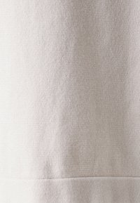 Lys beige stoff med en myk, teksturert overflate og et subtilt mønster. Materialet ser ut til å være vevd med en ren, strak kant nederst.
