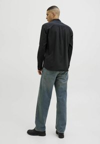 Tricou negru cu mânecă lungă, detalii evidente ale cusăturii, asortat cu blugi largi de culoare albastru deschis și cizme negre, privit din spate.