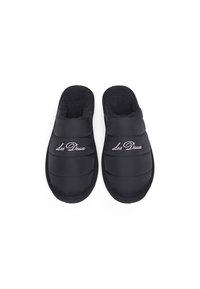 Black padded slippers with a soft interior lining, featuring "Les Deux" embroidered on the upper. Rounded shape and textured sole.