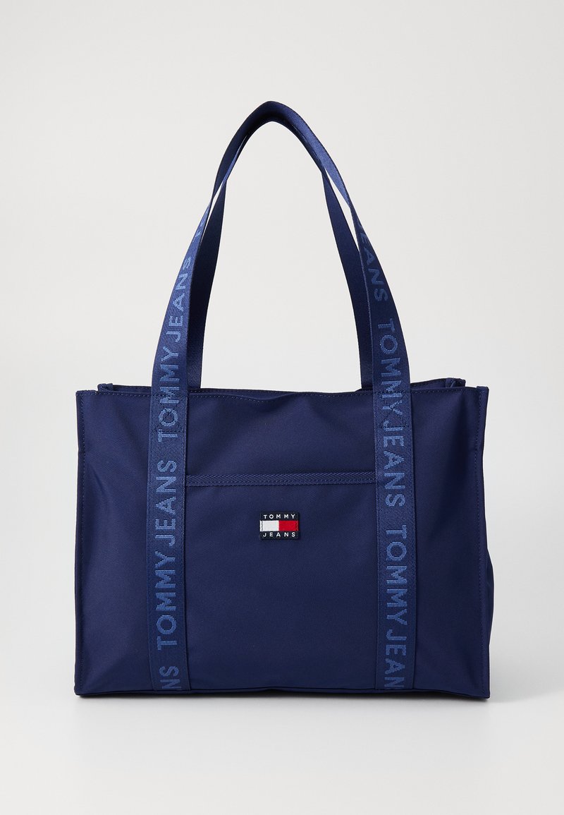 Tengerészkék nylon bevásárlótáska dupla füllel, elülső zsebbel és logóval. A pántok "TOMMY JEANS" felirattal díszítettek.