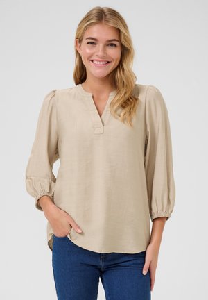Beige blouse with a V-neck and gathered 3/4 sleeves. Made from a lightweight fabric, featuring a curved hem and side pockets.