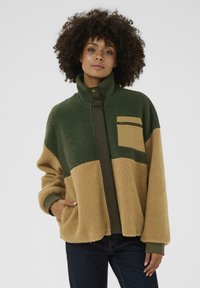 Giacca in fleece con blocchi di colore verde e beige, colletto alto, tasca frontale con zip e tasche foderate con polsini a coste.