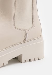Beige ankle boot made of smooth leather and fabric, featuring a chunky platform sole with a textured pattern, side elastic panels, and stitching details.