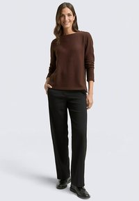 Pulover maro cu mâneci lungi și gât rotund, asortat cu pantaloni negri croiți și pantofi negri. Textură netedă, croială lejeră.