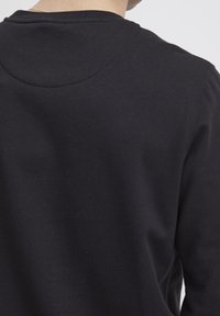 Felpa nera con collo arrotondato, morbida al tatto e con polsini a costine. La vista dal retro mostra un design semplice senza loghi o motivi.