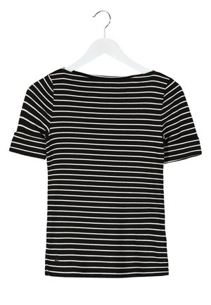 Femme portant un blazer beige, une chemise rayée noir et blanc, un pantalon beige et des bottes en cuir marron montant jusqu'aux genoux, marchant devant un fond uni.