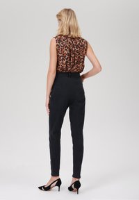 Top bez rukávů s leopardím vzorem v oranžové a černé, doplněný černými džínami s vysokým pasem, dokončený černými střevíčky na vysokém podpatku.