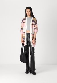Stickad cardigan med rosa, lila och beige randning; öppen framsida, långa ärmar. Bärs över en grå crop top och matchas med svarta utsvängda byxor.