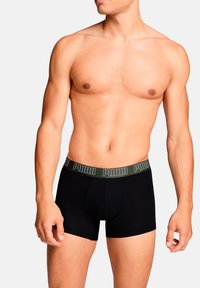 Schwarze Boxershorts mit einem grünen, markierten Bund, aus einem glatten, dehnbaren Stoff gefertigt. Oberschenkel-lange Schnittform mit eng anliegendem Sitz.