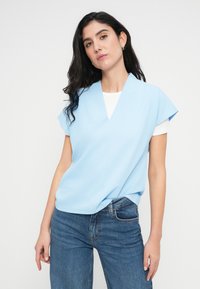 Ανοιχτό μπλε μπλουζάκι με κοντά μανίκια, V-λαιμόκοψη και άνετη εφαρμογή, σε συνδυασμό με μπλε jeans από τζιν υλικό. Ομαλή υφή, απλός σχεδιασμός χωρίς σχέδια.