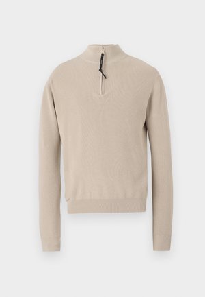 Beige gestrickter Pullover mit einem halben Reißverschlusskragen, gerippter Textur und langen Ärmeln. V-förmiges Design am Ausschnitt und schlichte Verarbeitung.
