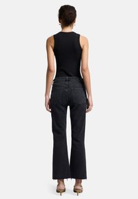 Schwarzes, geripptes Tanktop kombiniert mit hochtaillierten, schwarzen Denim-Jeans mit ausgestelltem Bein, die einen fransigen Saum und Gesäßtaschen mit gestickten Details haben.
