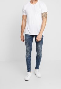 Camiseta blanca de manga corta combinada con pantalones vaqueros azules ajustados con detalles desgastados, complementada con zapatillas blancas.