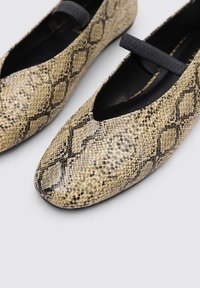 Ballerinas mit einem geometrischen Schlangenprint-Muster in Beige und Schwarz, mit einer abgerundeten Zehe und einem schwarzen elastischen Riemen über dem Spann.
