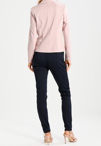 Lichtroze blazer met een getailleerd ontwerp, gecombineerd met marineblauwe op maat gemaakte broek. De blazer heeft een reverskraag en knoopaccenten.