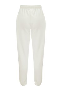 Białe dresy z miękkiej tkaniny, z elastycznym paskiem w talii, bocznymi kieszeniami oraz ściągaczami przy kostkach.