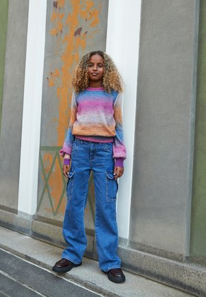 Colorful, knitted sweater with shades of blue, pink, and orange; paired with blue cargo jeans and dark brown platform shoes.