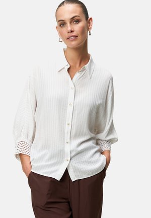 White button-up shirt with a textured fabric, featuring a collar and long sleeves with a detailed lace accent at the cuffs.