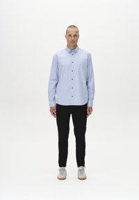 Light blue button-up shirt with a pocket and brown buttons, worn with black pants and gray sneakers featuring a cream sole.