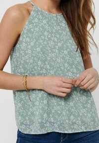 Débardeur vert clair à motif floral, doté d'un col licou et d'une coupe ample. Fabriqué en tissu doux et léger.