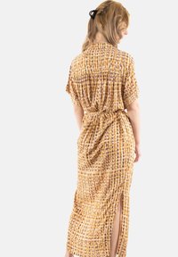 Vestido largo amarillo con un patrón texturizado de acentos morados y marrones. Presenta mangas cortas, una cintura ajustada y aberturas laterales.