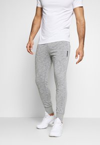 Grå sweatpants i en heathered tekstur med tætsiddende ben, afsluttende ankler og en sidelomme som accent. Sammen med en simpel hvid t-shirt og hvide sneakers.