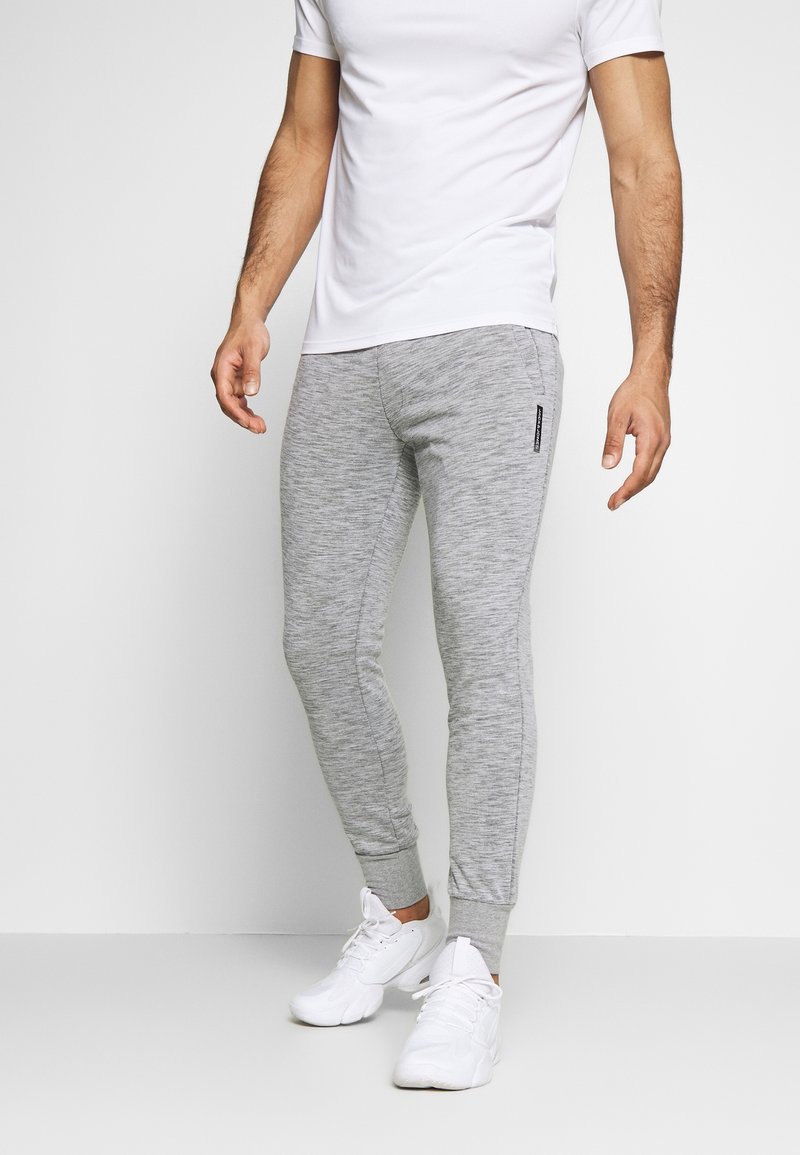 Grå sweatpants i en heathered tekstur med tætsiddende ben, afsluttende ankler og en sidelomme som accent. Sammen med en simpel hvid t-shirt og hvide sneakers.
