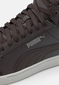 Braune Leder-Sneaker mit strukturierten Oberflächen, runder Zehenpartie, dicken Schnürsenkeln und einer weißen Gummisohle. Mit einem silbernen Puma-Logo.