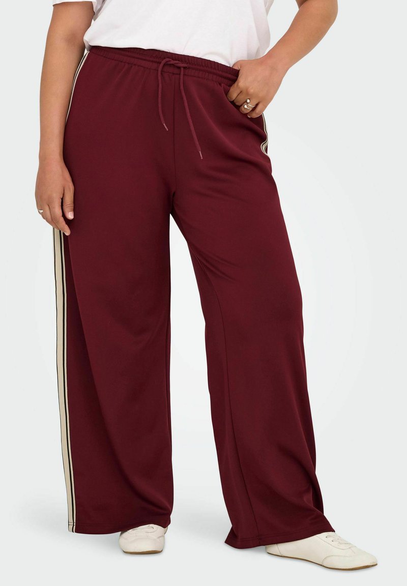 Tumši sarkanas plaša piegriezuma bikses ar atslābinātu pieguļojumu. Tām ir elastīga jostasvieta ar auklām un kontrastējošas baltas sānu svītras. Mīksta auduma tekstūra.