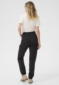 Svarta cargobyxor med elastiska avslut, sidofickor och hög midja, tillsammans med en ljusbeige T-shirt och beige sneakers.