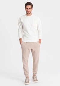 Hellbeige Sweatshirt mit Rundhalsausschnitt und Vordertasche, kombiniert mit hellbeigen tapered Pants mit seitlichen Taschen und beigen Sneakers.