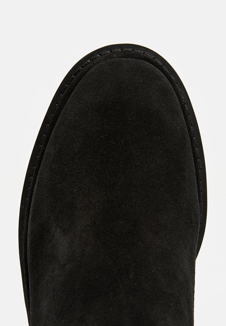 Schwarzer Wildleder-Absatzstiefelette mit abgerundetem Zehenbereich, sichtbaren Nähten und einer glatten Textur. Die Sohle ist leicht erhöht und passt sich der Fußform an.