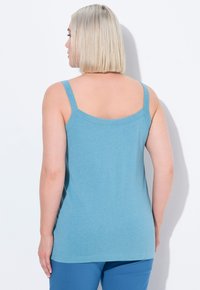 Top bluastro con spalline sottili, caratterizzato da una texture liscia e un collo arrotondato. La vista dalla schiena mette in risalto una vestibilità semplice e rilassata.